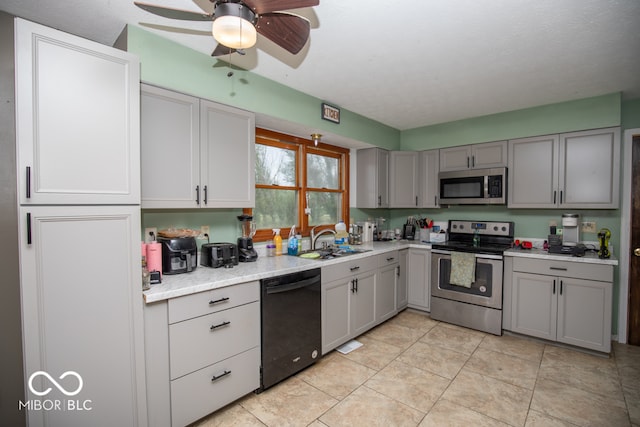 kitchen with appliances with stainless steel finishes, sink, gray cabinets, light tile patterned floors, and ceiling fan