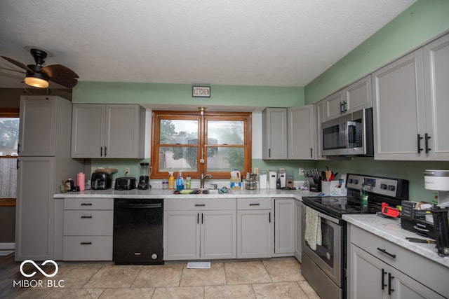 kitchen featuring ceiling fan, stainless steel appliances, sink, light tile patterned floors, and gray cabinetry