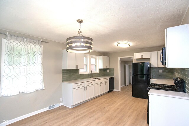 kitchen featuring white cabinetry, light hardwood / wood-style floors, black appliances, decorative light fixtures, and sink