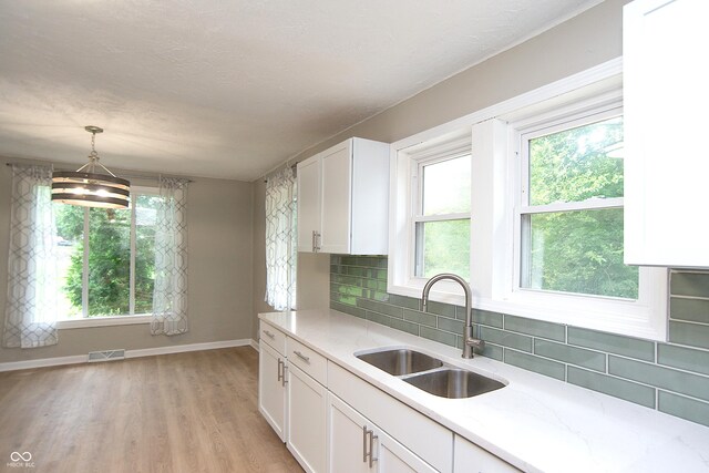 kitchen with decorative backsplash, white cabinets, light hardwood / wood-style flooring, sink, and decorative light fixtures