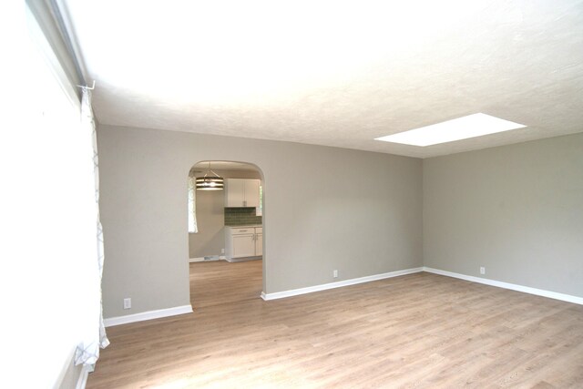 spare room featuring light wood-type flooring and a skylight