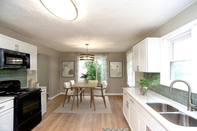 kitchen with light hardwood / wood-style flooring, backsplash, black appliances, sink, and decorative light fixtures