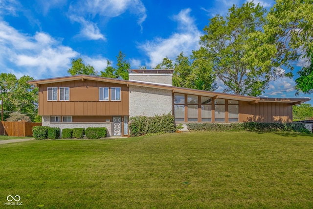 back of house featuring stone siding, a lawn, brick siding, and fence