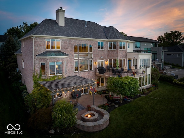 back house at dusk with a fire pit, a patio, a wooden deck, a yard, and a balcony