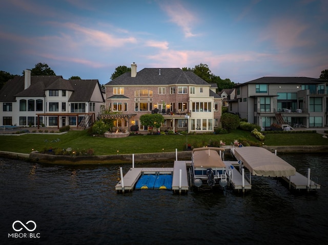 back house at dusk featuring a water view, a yard, and a balcony