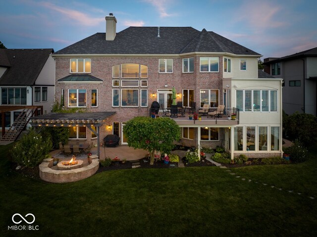 back house at dusk featuring a wooden deck, a pergola, a patio area, a fire pit, and a yard