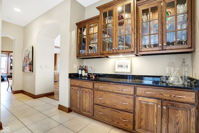 bar featuring dark stone counters, light tile patterned flooring, and sink