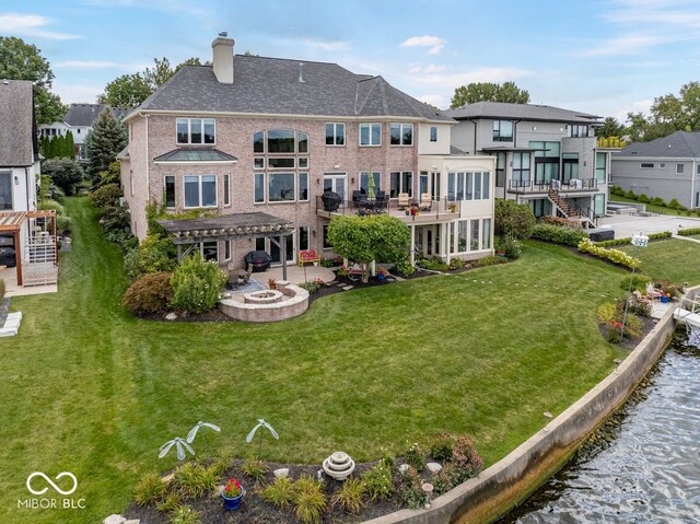 rear view of property featuring a pergola, a patio, an outdoor fire pit, a water view, and a yard