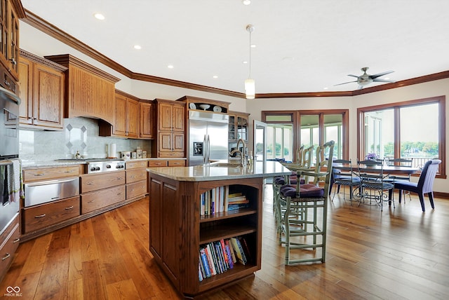 kitchen featuring appliances with stainless steel finishes, hanging light fixtures, an island with sink, crown molding, and wood-type flooring