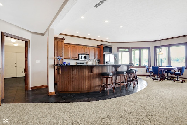 kitchen featuring ornamental molding, dark colored carpet, stainless steel appliances, and a kitchen bar