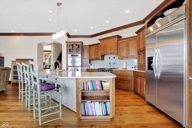 kitchen with light wood-type flooring, stainless steel appliances, a center island with sink, decorative light fixtures, and crown molding