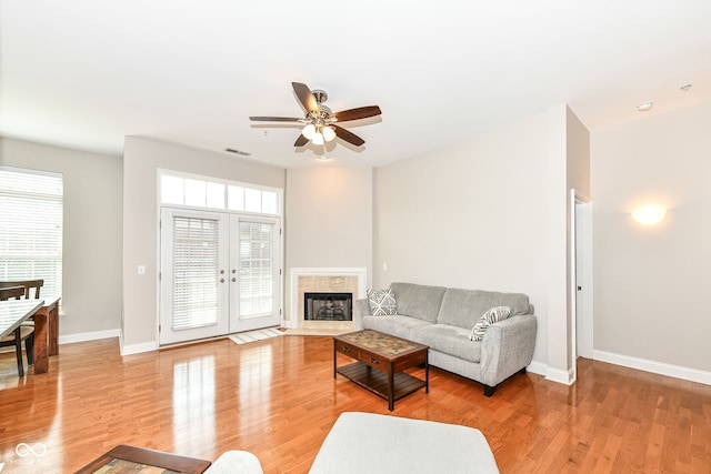 living room with french doors, ceiling fan, a fireplace, and light wood-type flooring