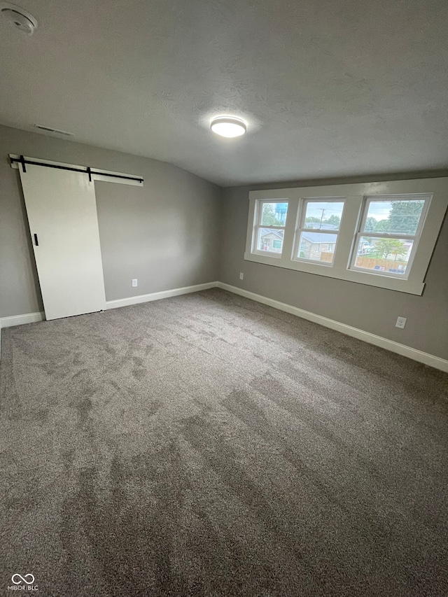 unfurnished bedroom featuring a barn door, carpet floors, and a textured ceiling