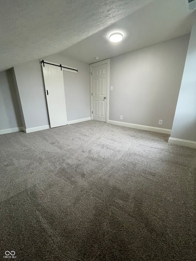 unfurnished bedroom with a barn door, carpet, and a textured ceiling