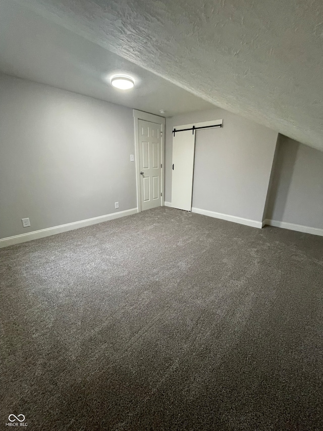 unfurnished bedroom with a barn door, carpet floors, and a textured ceiling