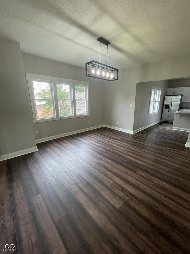 unfurnished dining area with a textured ceiling, a chandelier, and dark wood-type flooring