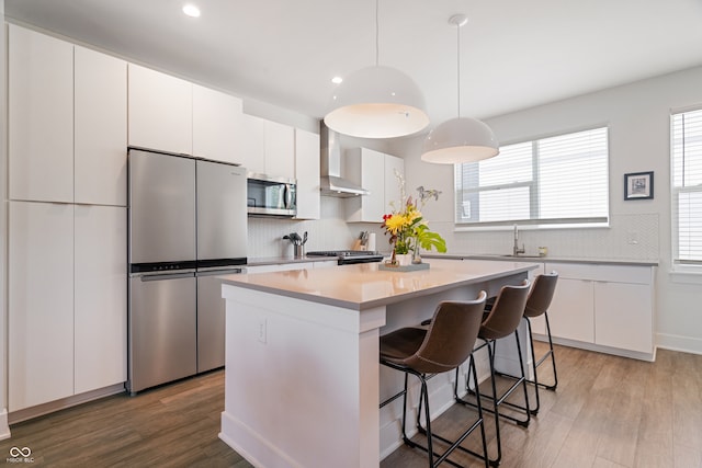 kitchen with stainless steel appliances, hardwood / wood-style floors, backsplash, a center island, and wall chimney exhaust hood