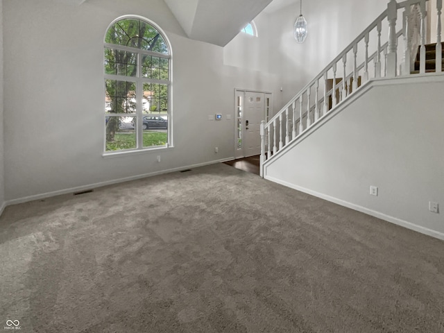 unfurnished living room featuring an inviting chandelier, high vaulted ceiling, and dark carpet