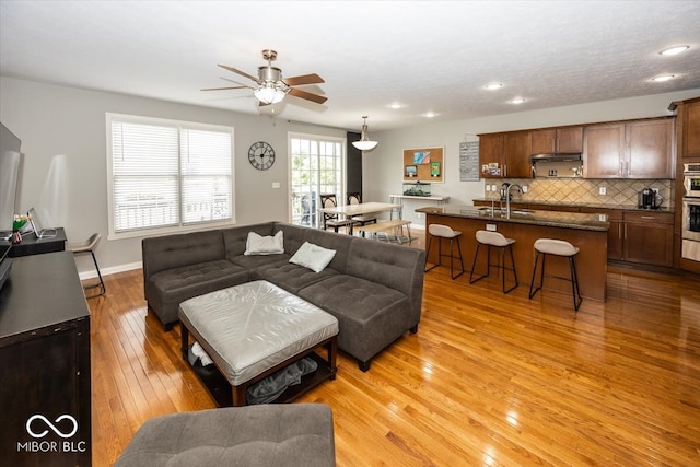 living room featuring ceiling fan, sink, and light wood-type flooring