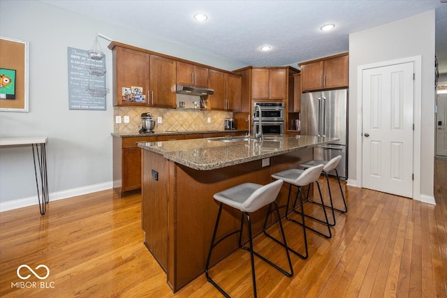 kitchen featuring a kitchen bar, appliances with stainless steel finishes, a kitchen island with sink, light hardwood / wood-style floors, and backsplash