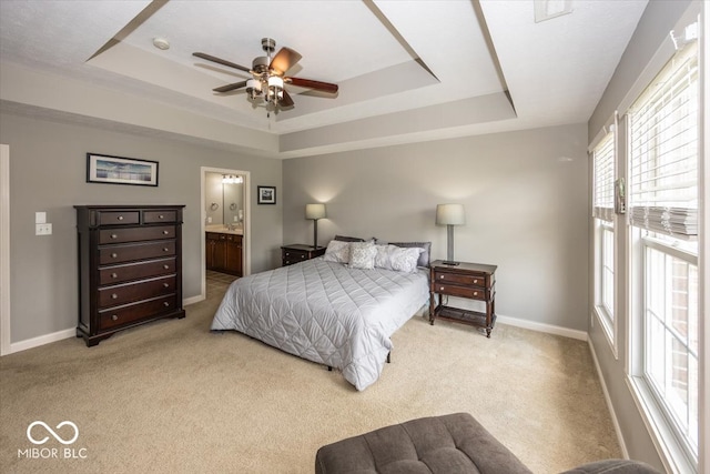 carpeted bedroom featuring ceiling fan, ensuite bath, and a tray ceiling