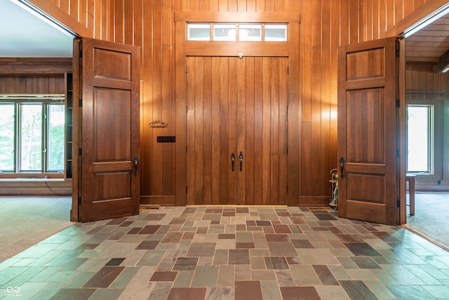 foyer entrance featuring wood walls and dark colored carpet