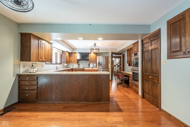 kitchen with kitchen peninsula, light hardwood / wood-style floors, light stone countertops, appliances with stainless steel finishes, and decorative light fixtures