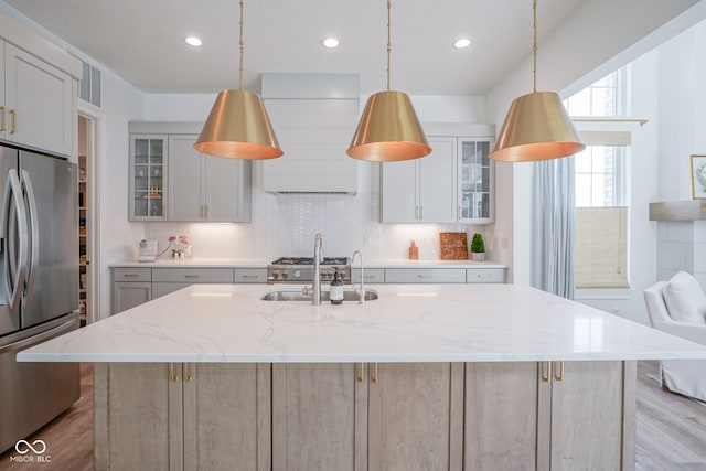 kitchen with tasteful backsplash, a center island with sink, premium range hood, light hardwood / wood-style floors, and stainless steel refrigerator with ice dispenser