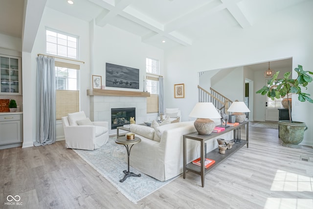 living room featuring beamed ceiling, light hardwood / wood-style flooring, coffered ceiling, and a tiled fireplace