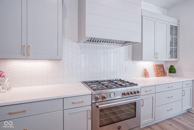 kitchen with high end range, light hardwood / wood-style flooring, tasteful backsplash, and premium range hood