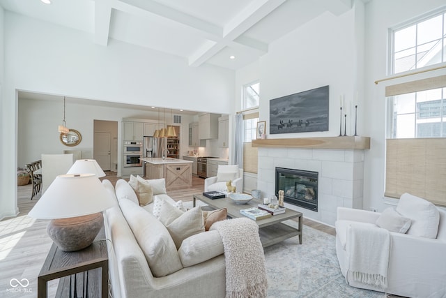 living room featuring a high ceiling, sink, beam ceiling, light hardwood / wood-style flooring, and a tiled fireplace