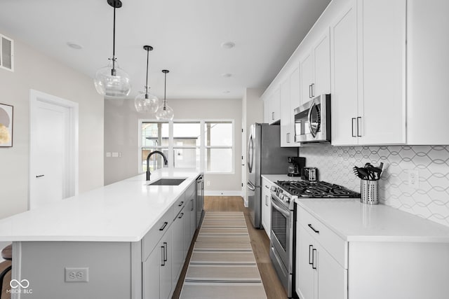 kitchen featuring white cabinetry, stainless steel appliances, decorative light fixtures, and an island with sink