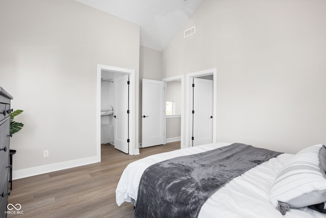 bedroom with light hardwood / wood-style floors, a walk in closet, high vaulted ceiling, and a closet