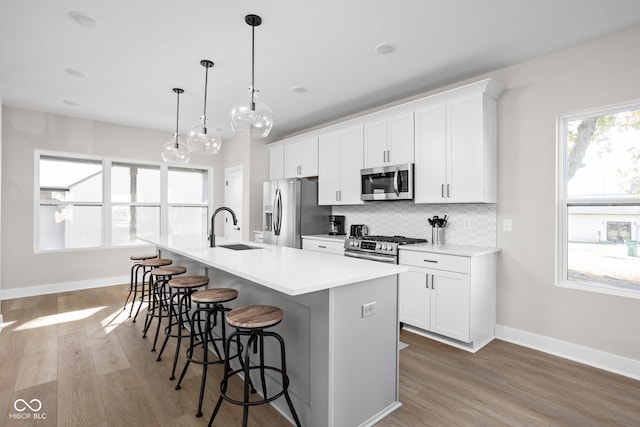 kitchen with a breakfast bar, pendant lighting, white cabinets, stainless steel appliances, and a center island with sink