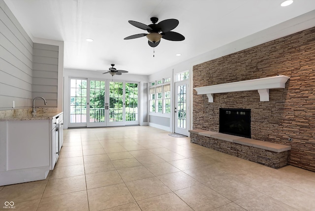 unfurnished living room featuring light tile patterned floors, a fireplace, sink, and ceiling fan