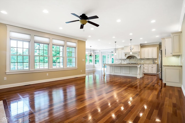 unfurnished living room with crown molding, recessed lighting, ceiling fan with notable chandelier, baseboards, and dark wood-type flooring
