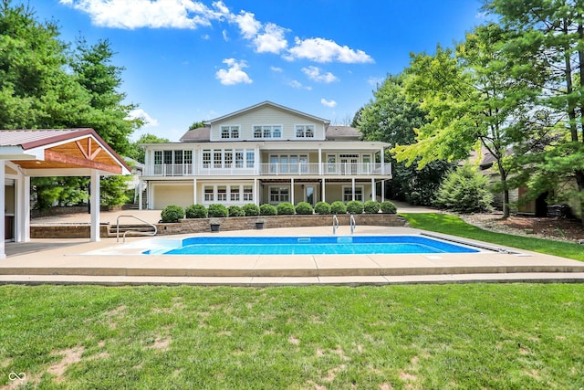 rear view of property featuring an outdoor pool, a balcony, a yard, and a patio area
