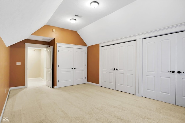 unfurnished bedroom featuring multiple closets, carpet floors, baseboards, and vaulted ceiling