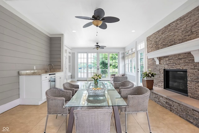 dining area featuring ceiling fan, wood walls, sink, light tile patterned floors, and a fireplace