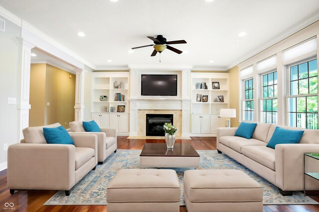 living room with ceiling fan, ornamental molding, light hardwood / wood-style flooring, a tiled fireplace, and ornate columns