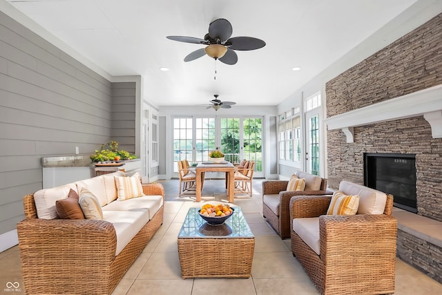 tiled living room with wood walls, ceiling fan, and a stone fireplace