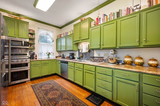 kitchen with appliances with stainless steel finishes, light wood-type flooring, crown molding, sink, and green cabinets