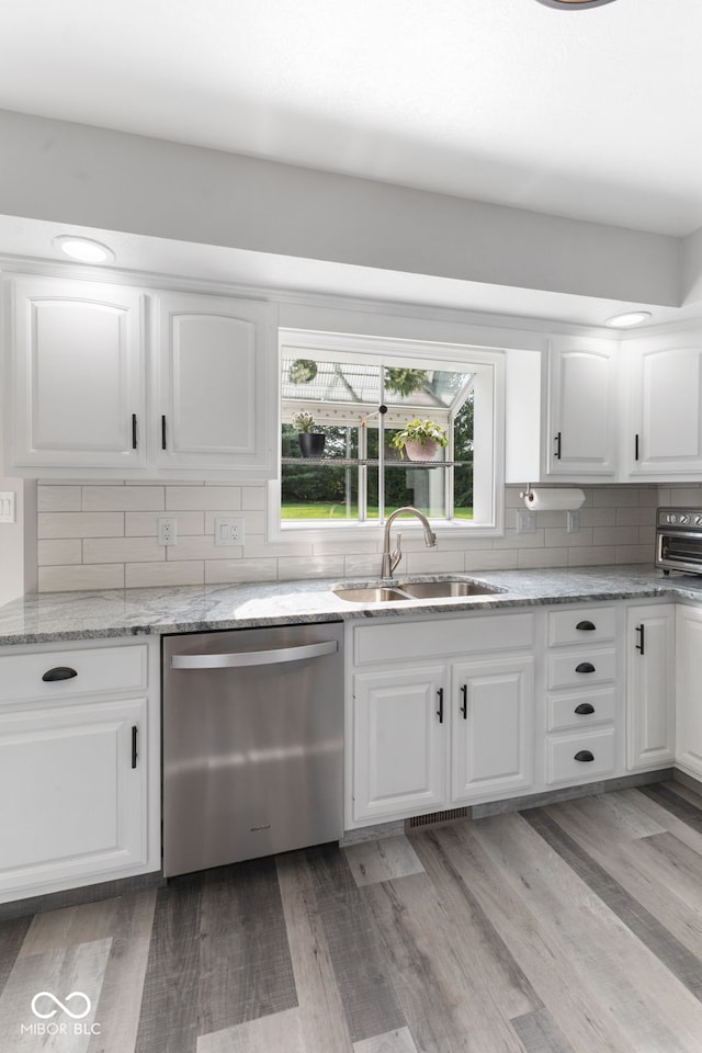 kitchen featuring light wood-type flooring, decorative backsplash, stainless steel dishwasher, sink, and white cabinets