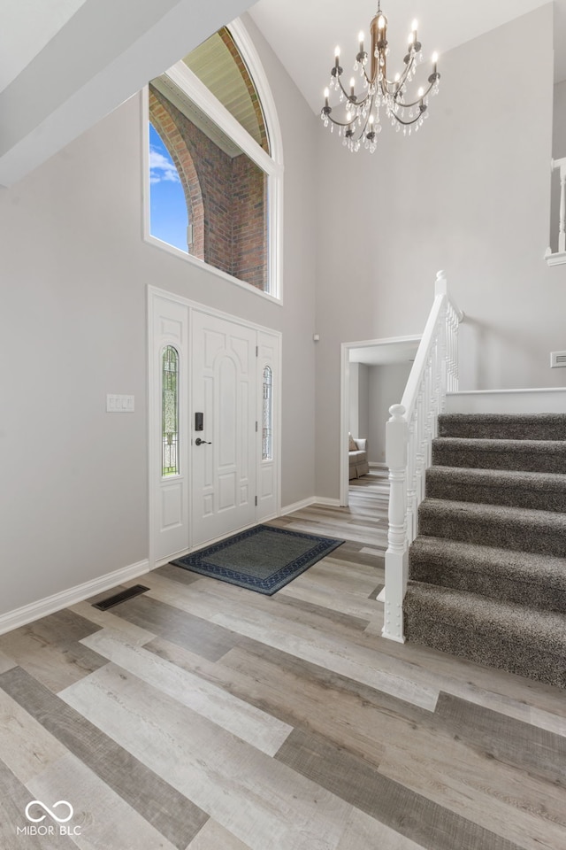 entryway featuring light wood-type flooring, high vaulted ceiling, and an inviting chandelier