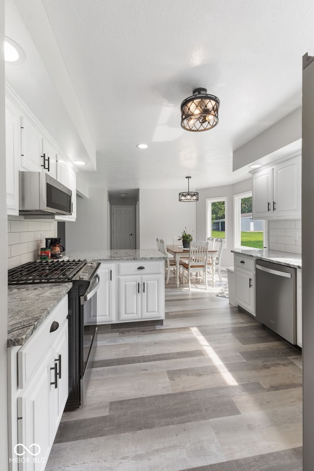 kitchen with white cabinets, backsplash, stainless steel appliances, and light hardwood / wood-style flooring