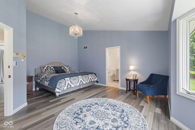 bedroom with connected bathroom, vaulted ceiling, a chandelier, and hardwood / wood-style flooring