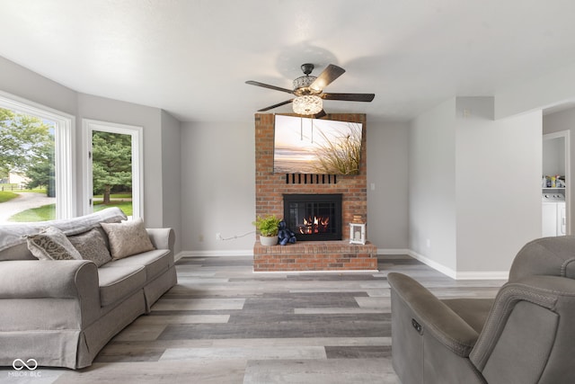 living room with ceiling fan, a fireplace, hardwood / wood-style flooring, and brick wall