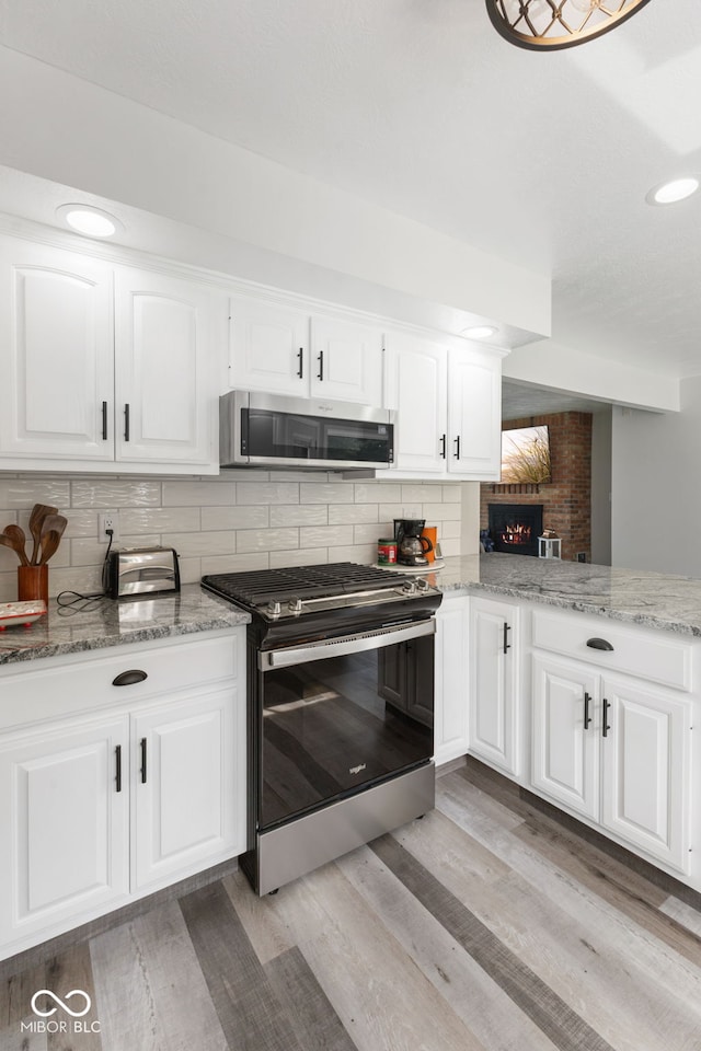 kitchen featuring tasteful backsplash, light hardwood / wood-style flooring, stainless steel appliances, and brick wall