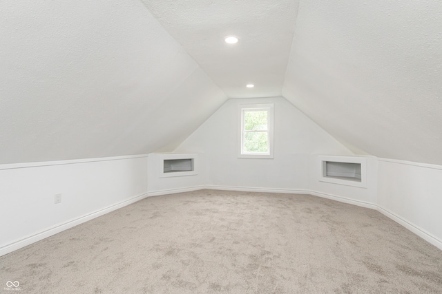 bonus room with a textured ceiling, light colored carpet, and vaulted ceiling