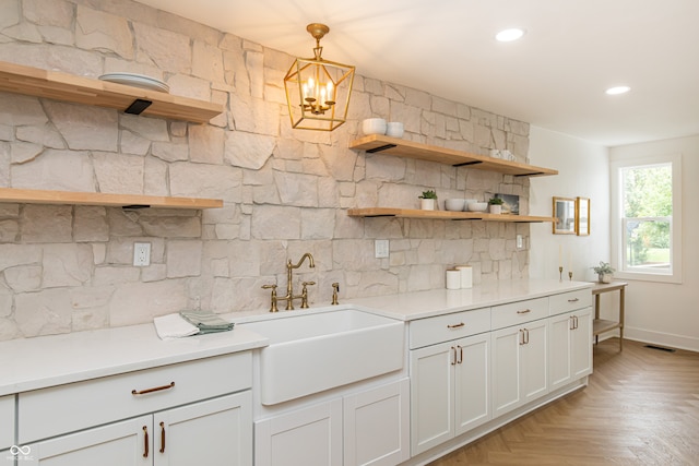 kitchen with a notable chandelier, light parquet floors, pendant lighting, white cabinets, and sink